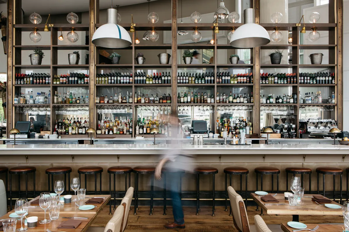 A run of leather-topped stools along a marble bar under open shelving